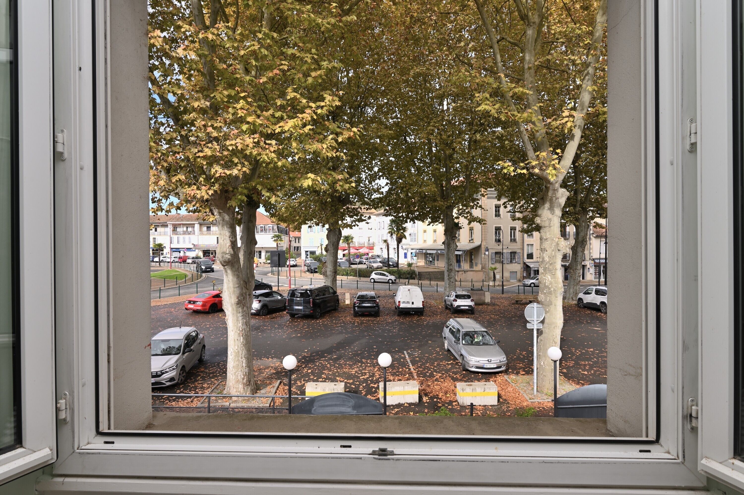 A view through a window of a parking lot with trees and buildings in the background.