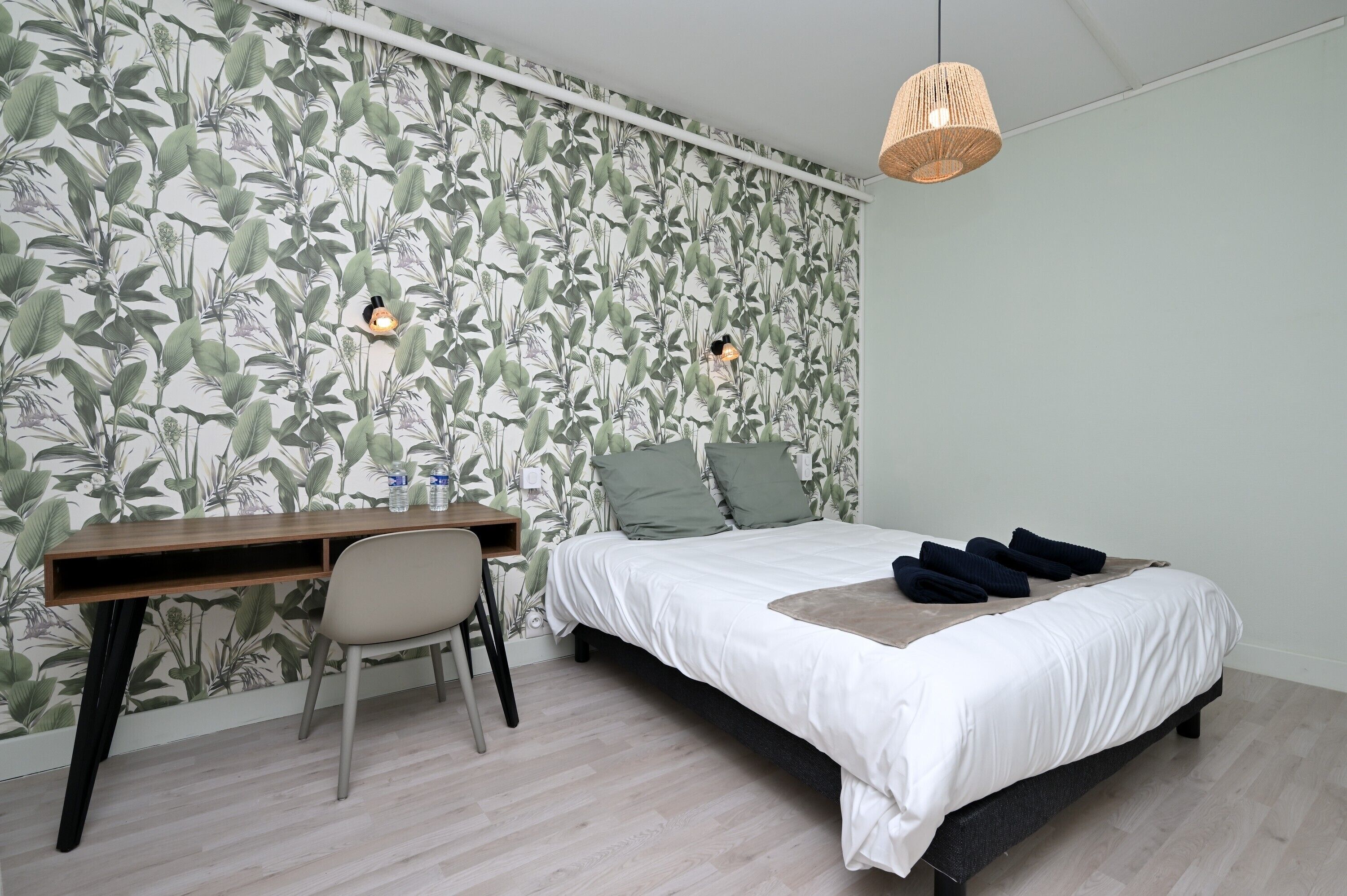 Een slaapkamer met een bed, bureau, stoel en een muur met een bladerpatroon.