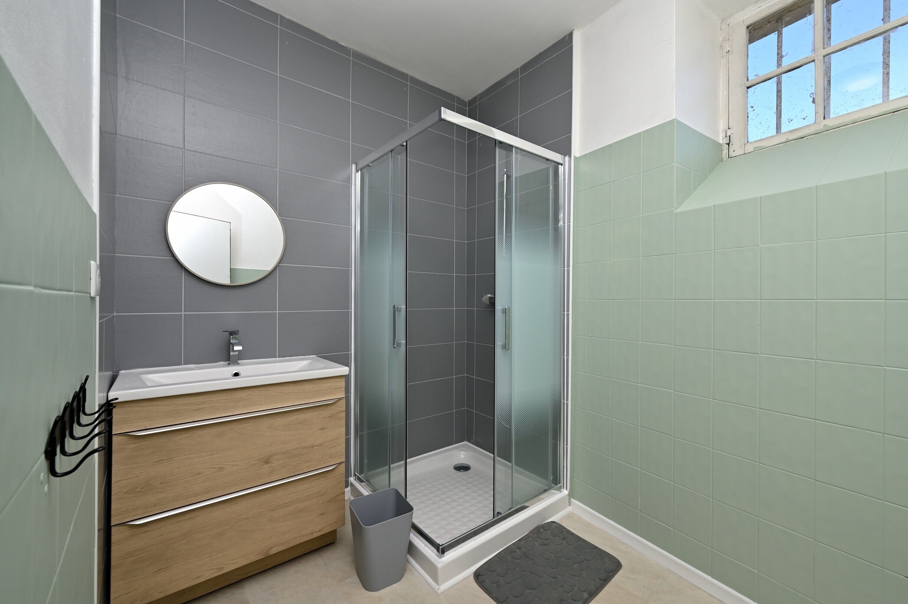 A modern bathroom with a glass shower enclosure, a round mirror, and a wooden vanity.