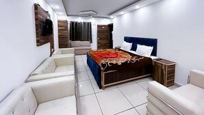 A modern bedroom with a large bed, a seating area, and a wardrobe. - Roomshala J S Garden (Noida)