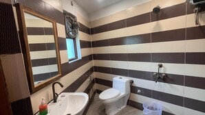 A bathroom with a sink, two toilets, a mirror, and striped tiles. - Roomshala J S Garden (Noida)