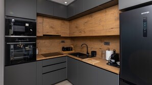 A modern kitchen with grey cabinetry, wooden accents, a built-in oven, a sink, and a black refrigerator.