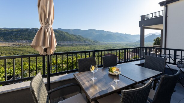 A balcony with a table set for two, overlooking a mountainous landscape.