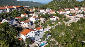 An aerial view of a residential area with houses, a swimming pool, and a hilly landscape in the background.