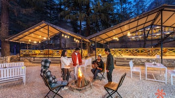 An outdoor seating area with a fire pit, white chairs, and tables under a covered structure.