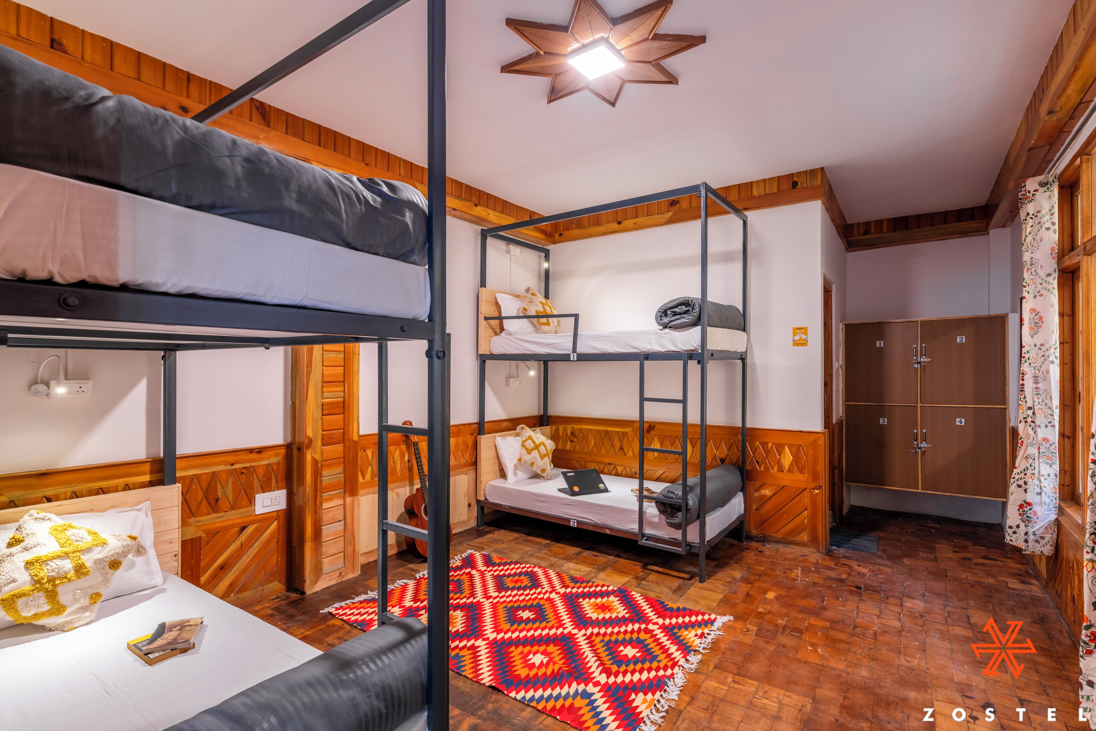 A dormitory-style room with bunk beds, a wooden floor, a star-shaped ceiling light, and a wardrobe with two doors.