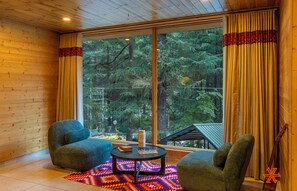 A cozy room with wooden walls, a large window with curtains, two armchairs, a small table with a chessboard, and a guitar leaning against the wall. - Zostel Kasol (Main Market) (Kasol)
