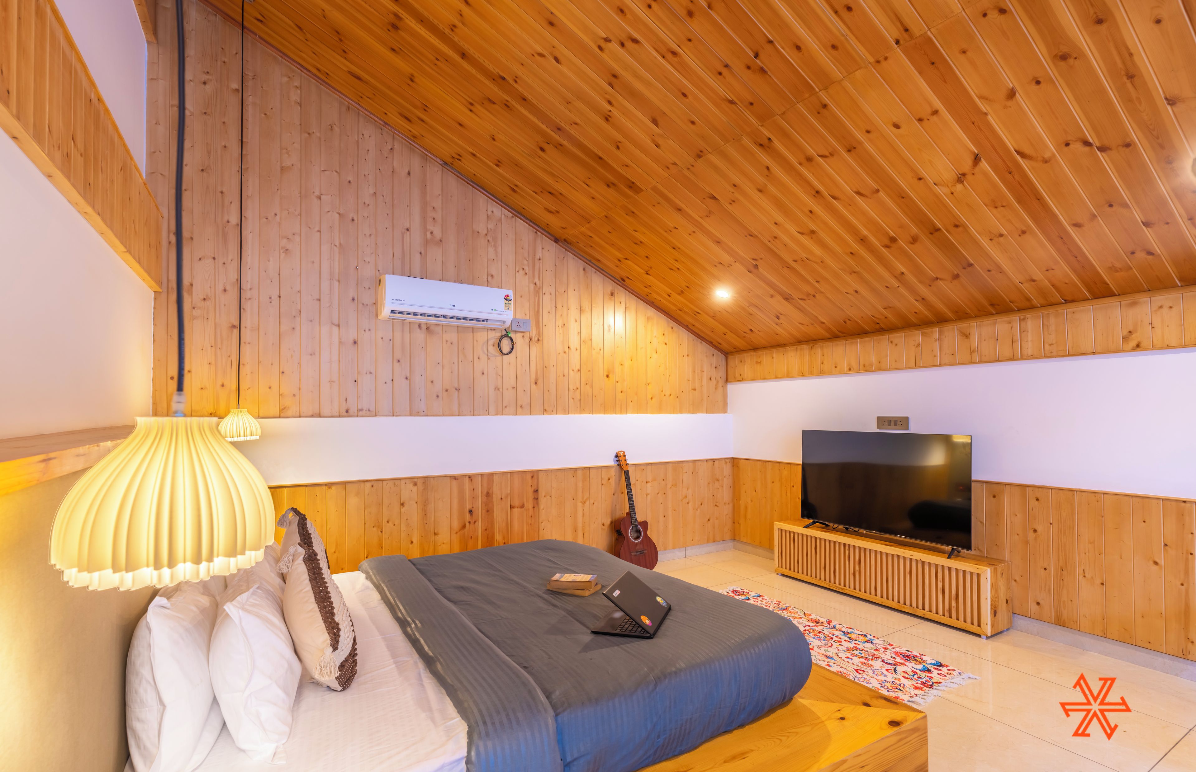 A bedroom with a wooden ceiling, a bed with pillows, a guitar, a TV, and a radiator.