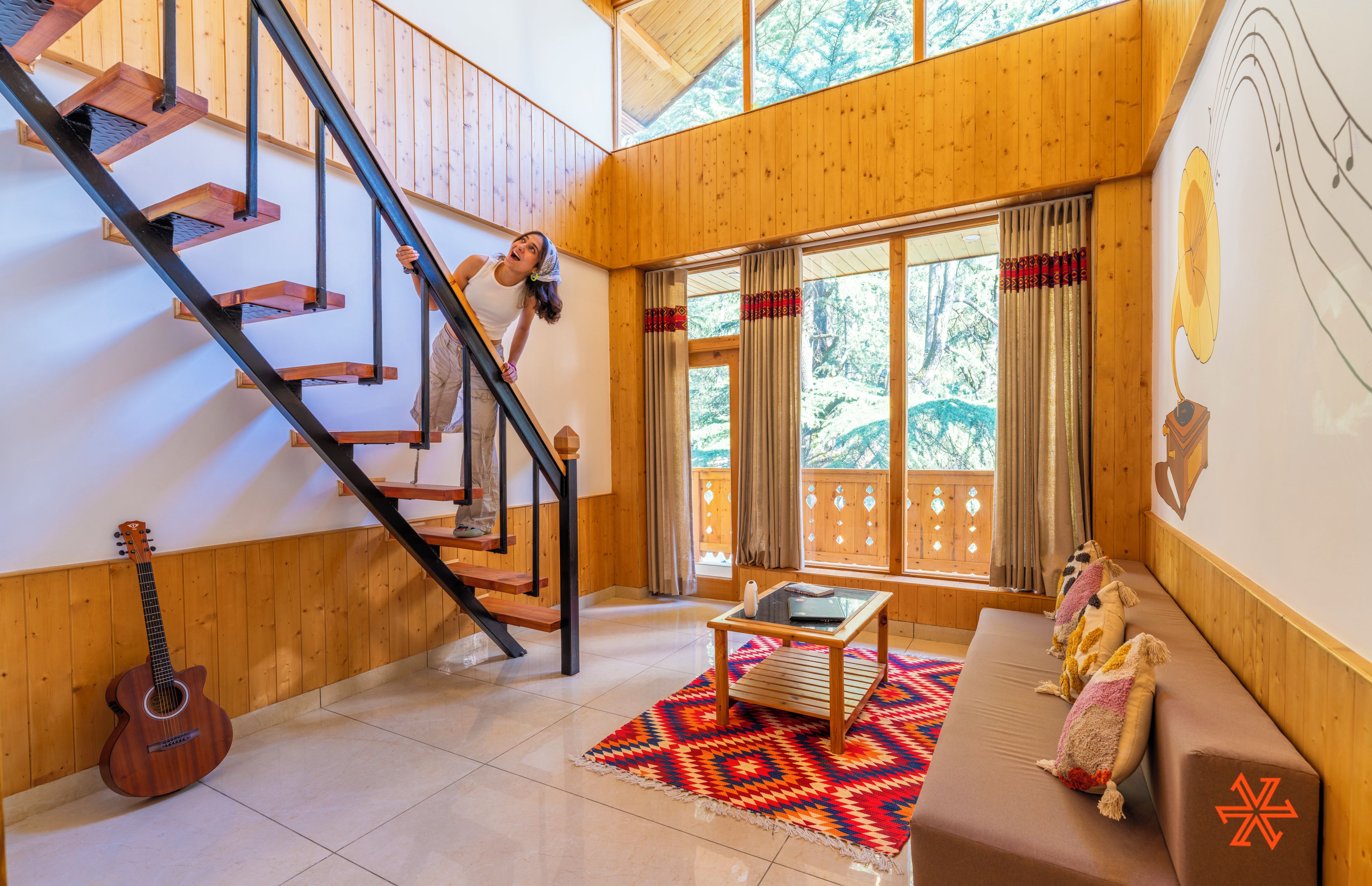 A wooden interior with a staircase, a sofa, a table, and a guitar.