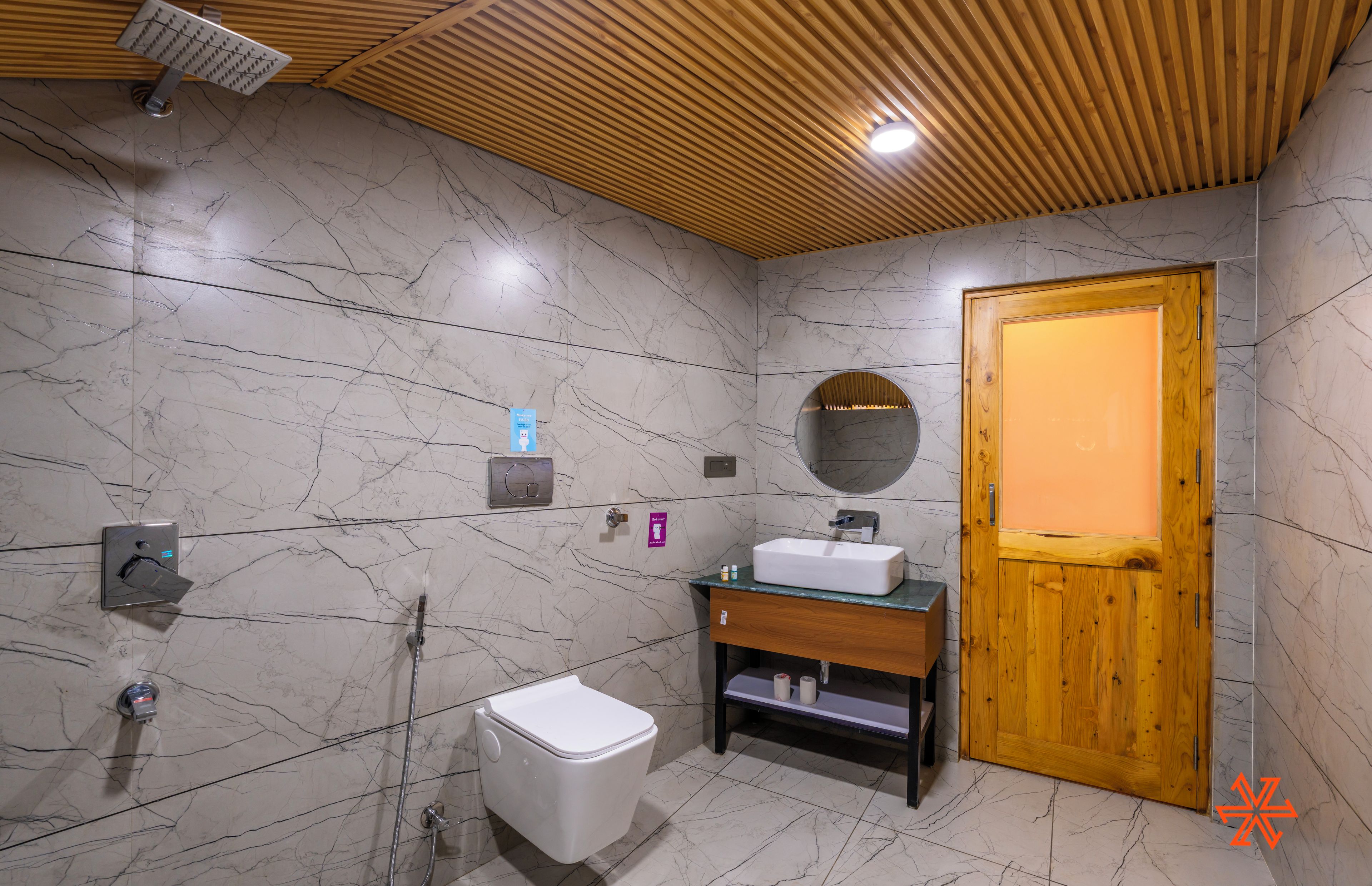 A modern bathroom with a wooden ceiling, marble walls, a wooden door, a sink, and a toilet.