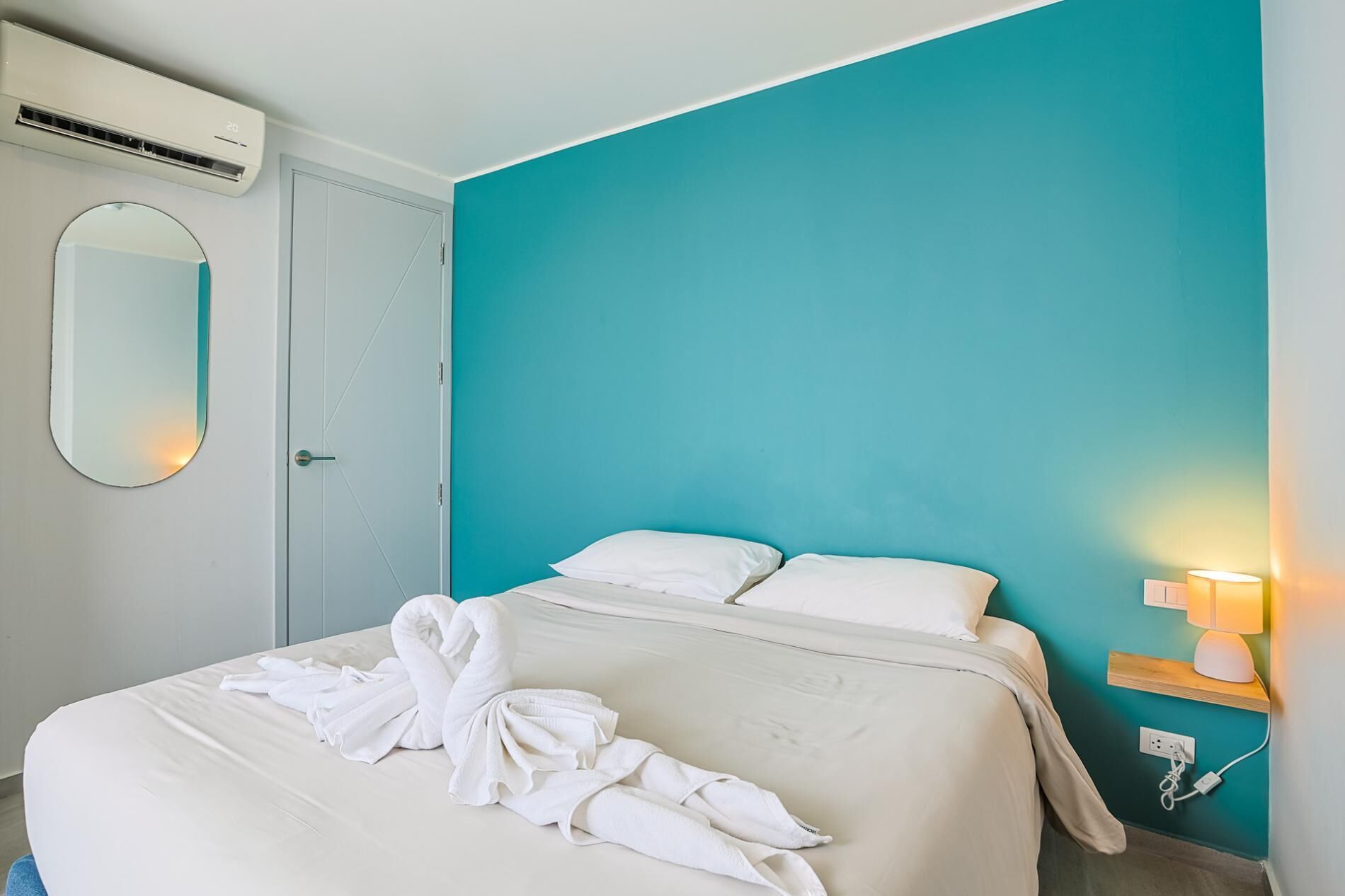 Et hotelværelse med en seng, et spejl, aircondition og en væg i teal farve.