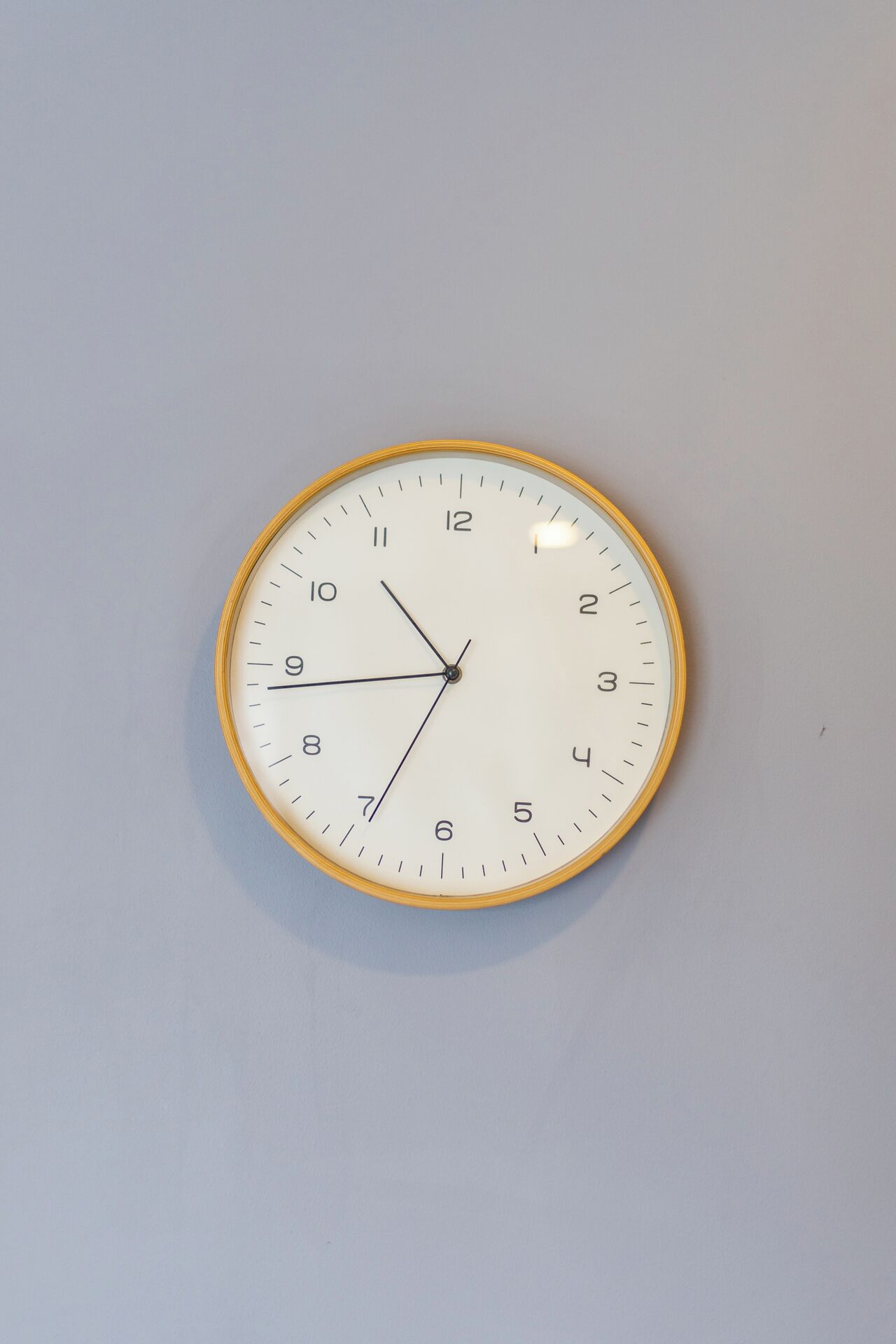 A round wall clock with a white face and yellow rim, mounted on a plain wall.