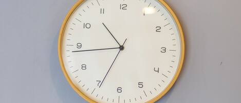 A round wall clock with a white face and yellow rim, mounted on a plain wall.