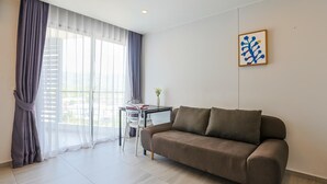 A modern living room with a sofa, a dining table, and a chair. There is a window with sheer curtains and a view of the outside. - Mountain View 1 Bed Apt T2-723 (Chalong)
