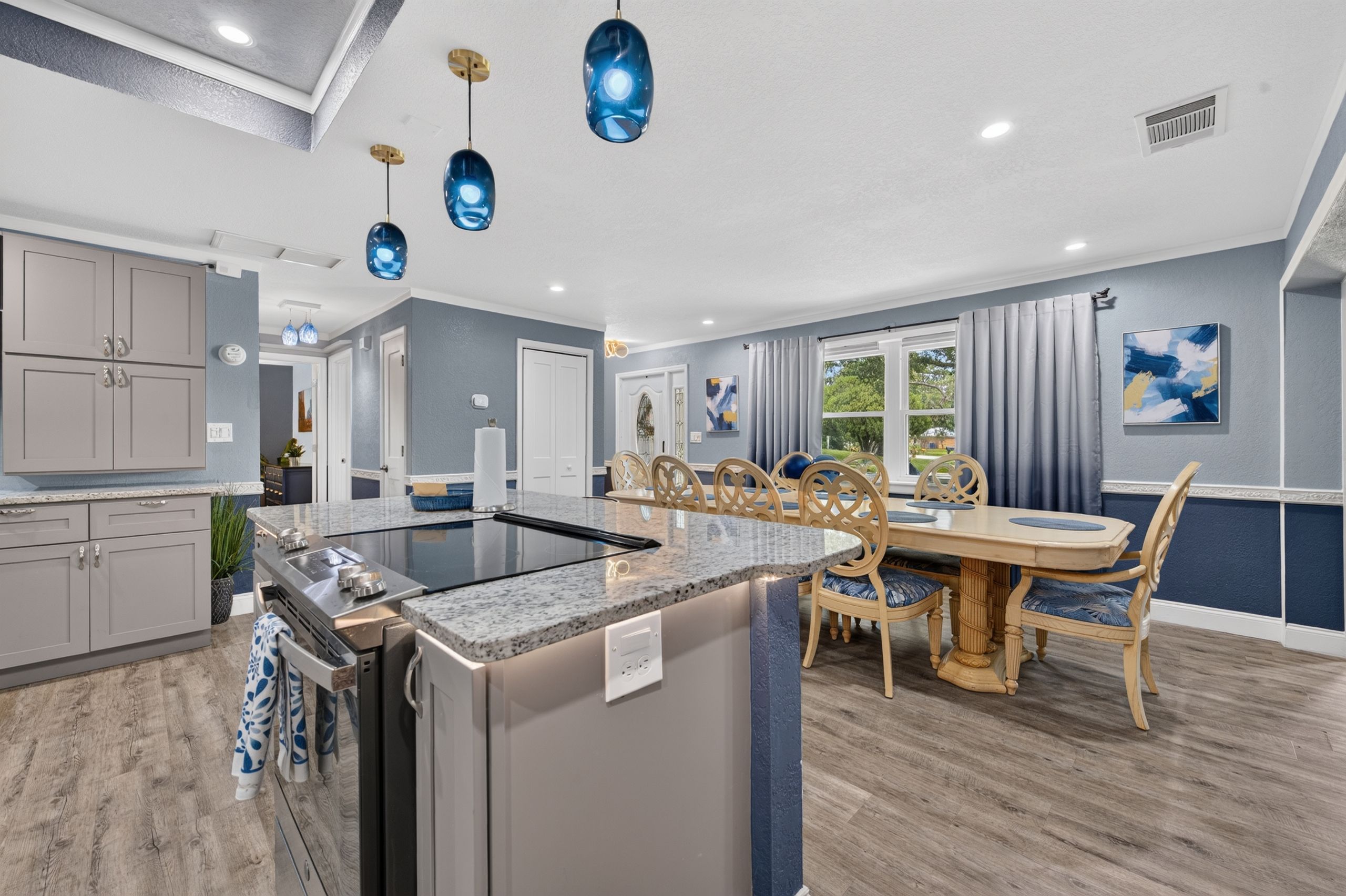 A modern kitchen with a central island, a dining area with a wooden table and chairs, and a living space with a view of the outdoors.