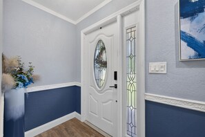 Ein Flur mit einer weißen Tür, einem farbigen Glasfenster und einem an der Wand befestigten Lichtschalter.