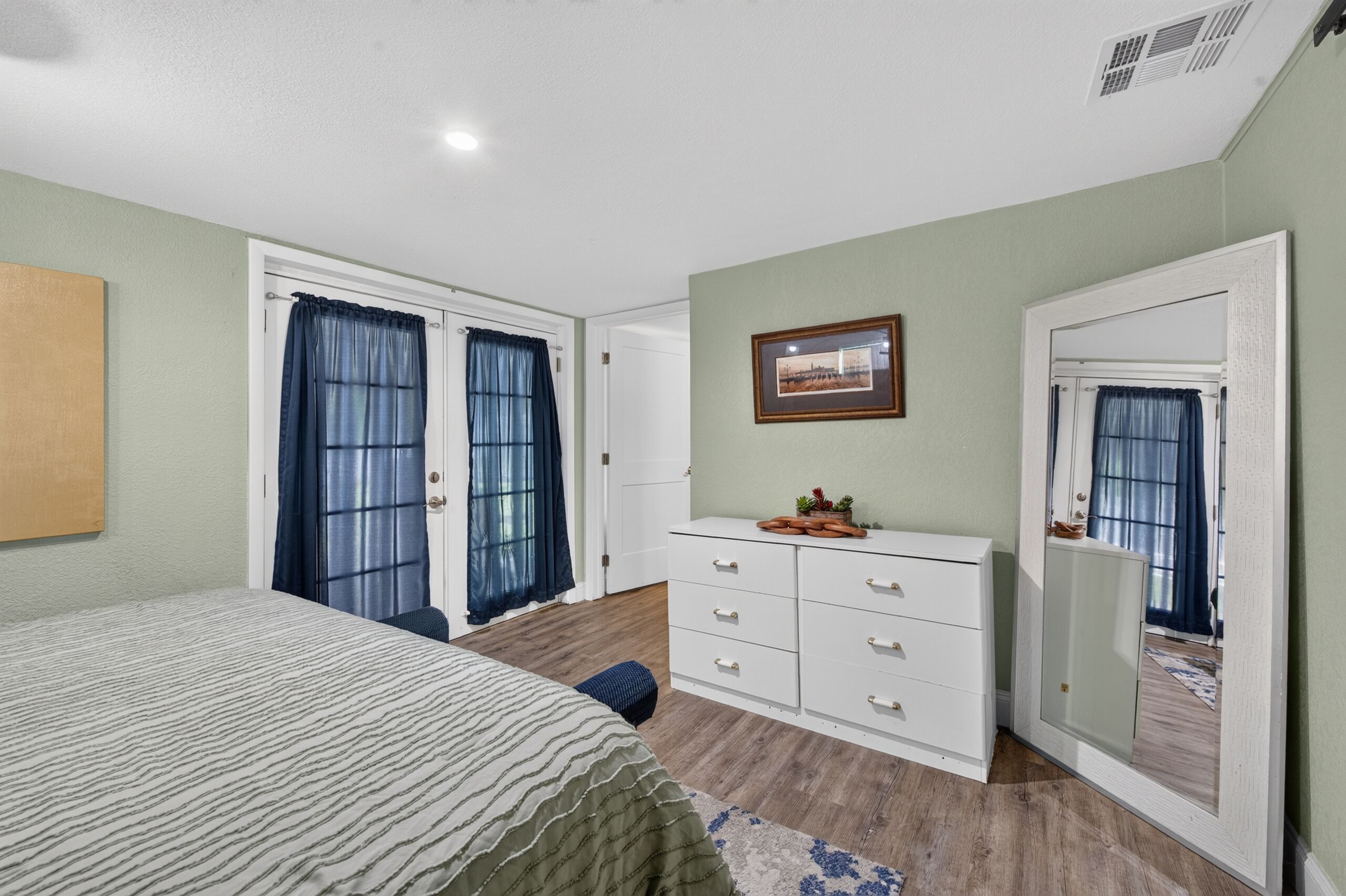 A bedroom with a bed, a dresser, a mirror, and a door with curtains.