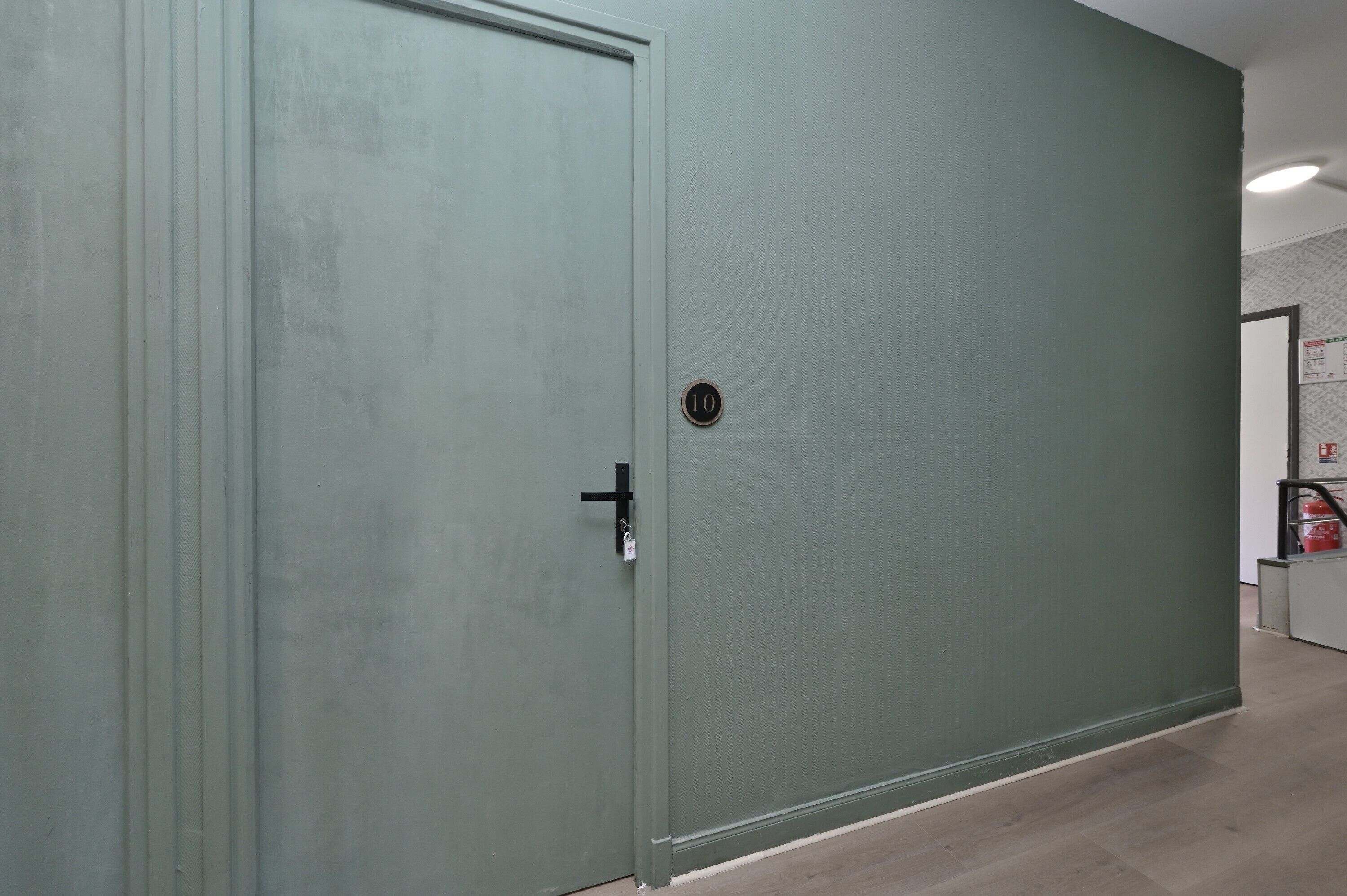 Une porte fermée avec une plaque numérotée, un extincteur et un mur orné d’un motif.