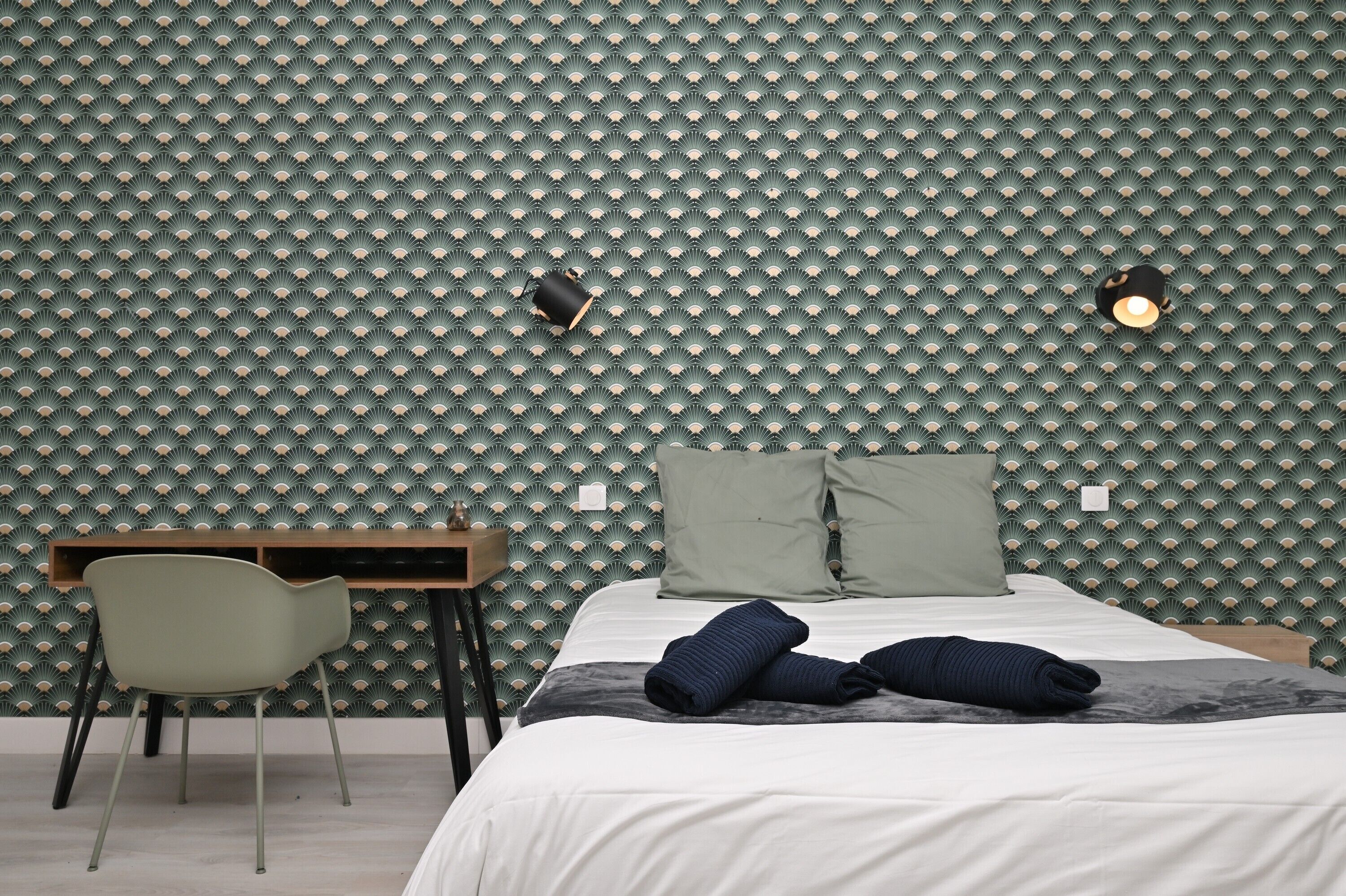 Een kamer met een behang, een bed met kussens, een bureau en een stoel.