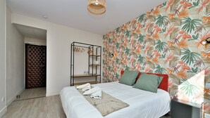 Een slaapkamer met een bed, nachtkastje, kledingkast en een muur met een tropisch bladpatroon.