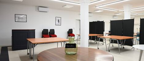 Un salón de conferencias con mesas, sillas y una mesa central con un jarrón decorativo.