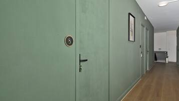 Un couloir aux murs verts, avec un plancher en bois et des portes portant des numéros.