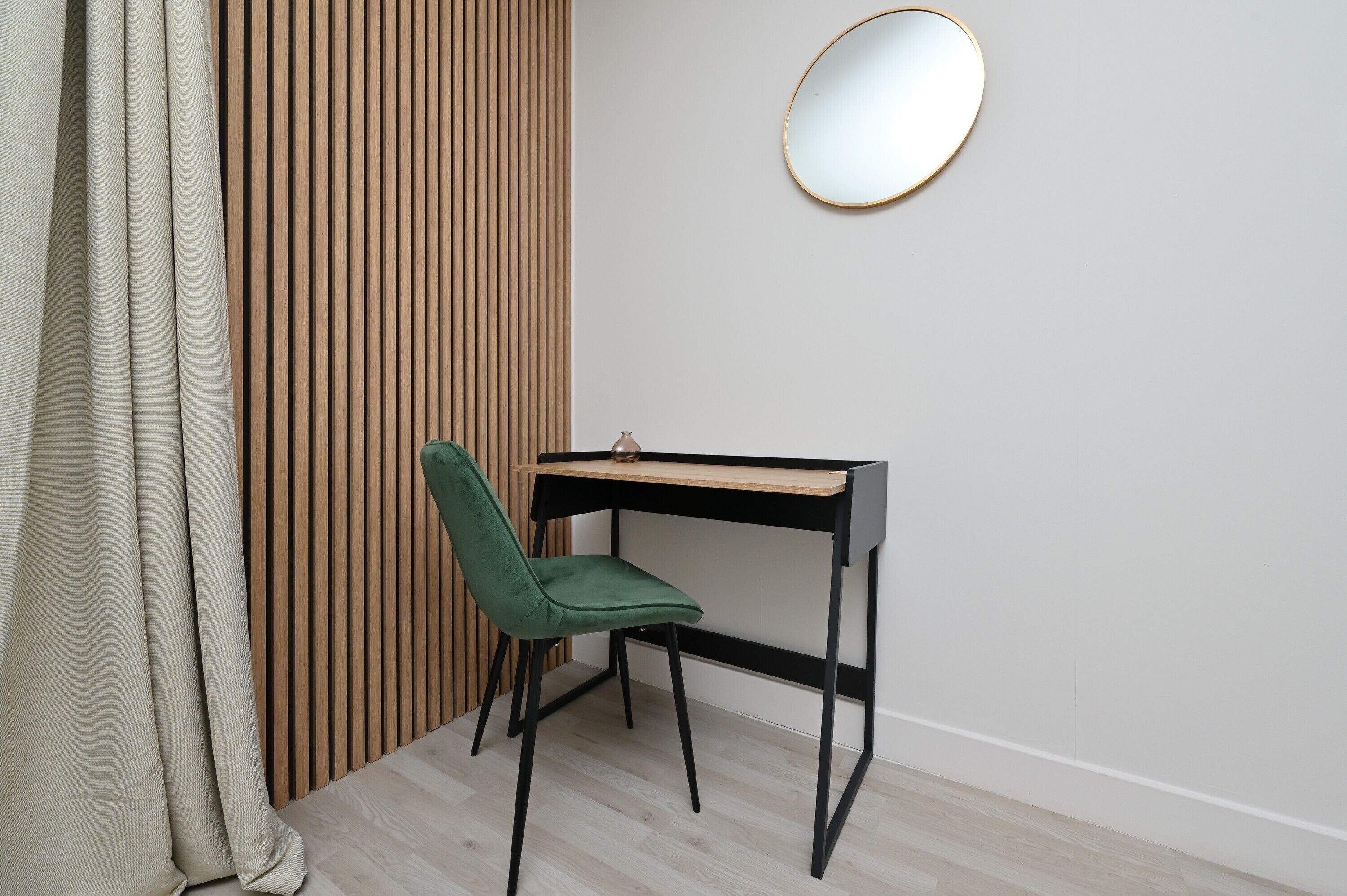 Una habitación con pared de listones de madera, un escritorio con silla y un espejo redondo en la pared.
