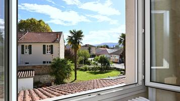 Une vue depuis une fenêtre donnant sur un quartier résidentiel, avec des maisons, un palmier et un ciel dégagé.