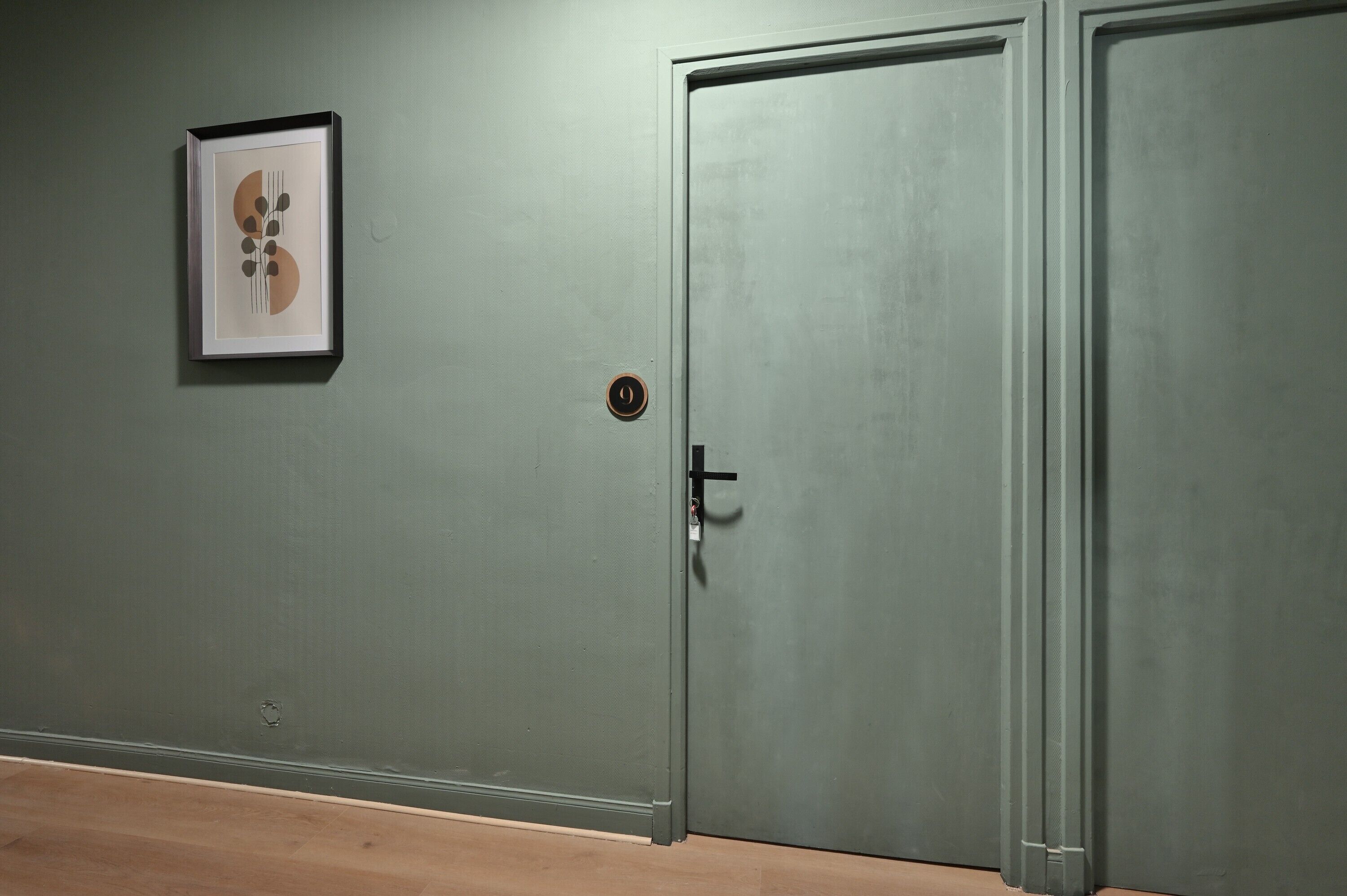 Una puerta cerrada con cerradura y un ojo de cerradura, un cuadro enmarcado en la pared y un suelo de madera.