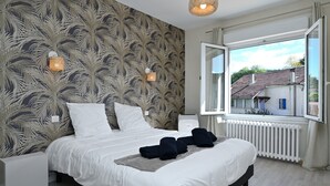 Een slaapkamer met een bed, twee wandlampen, een raam met uitzicht op gebouwen en een radiator.