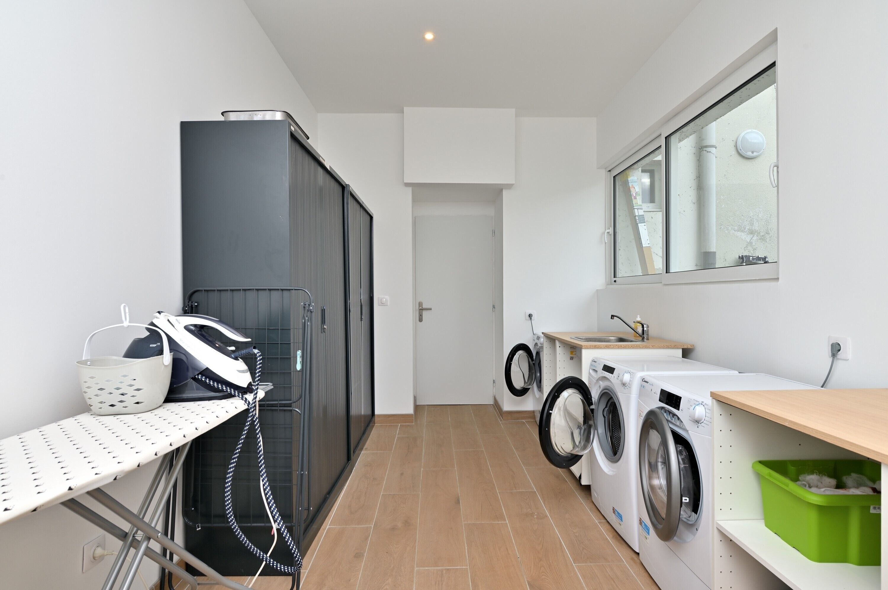 A laundry room with a washing machine, dryer, ironing board, and a drying rack.