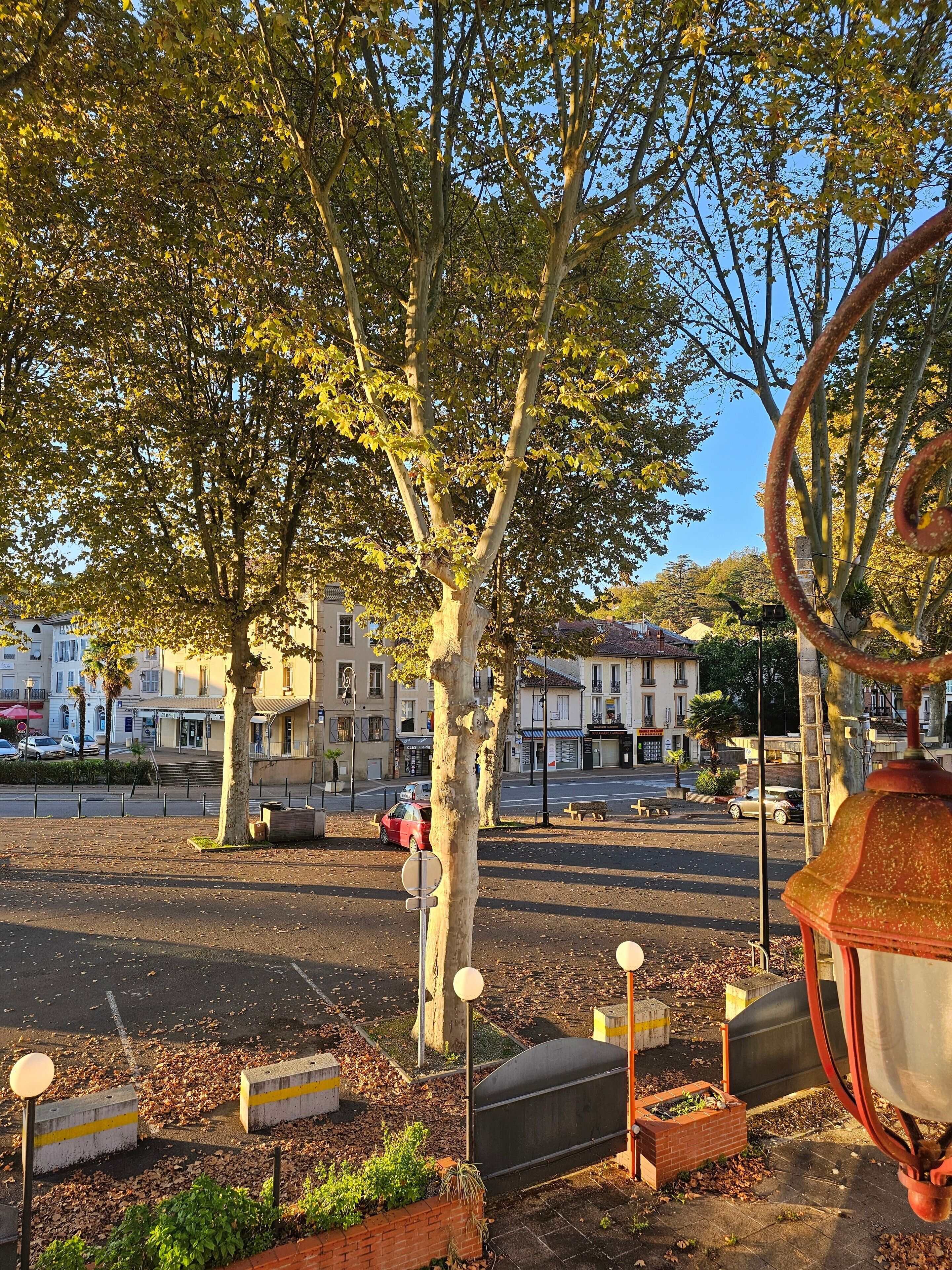 A public square with trees, benches, and a red taxi.