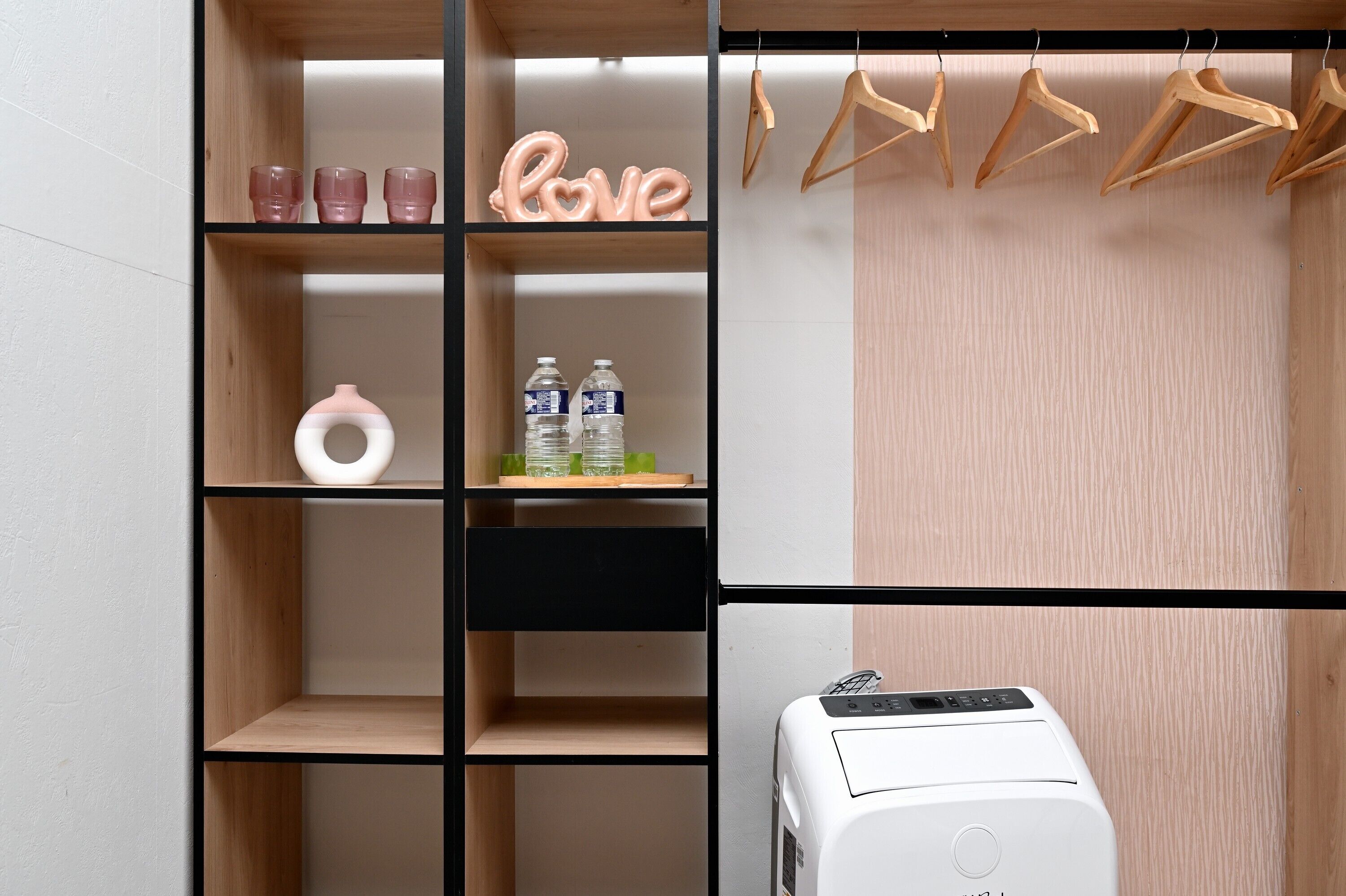Un armario con estantes de madera, una barra para colgar ropa y un electrodoméstico blanco.