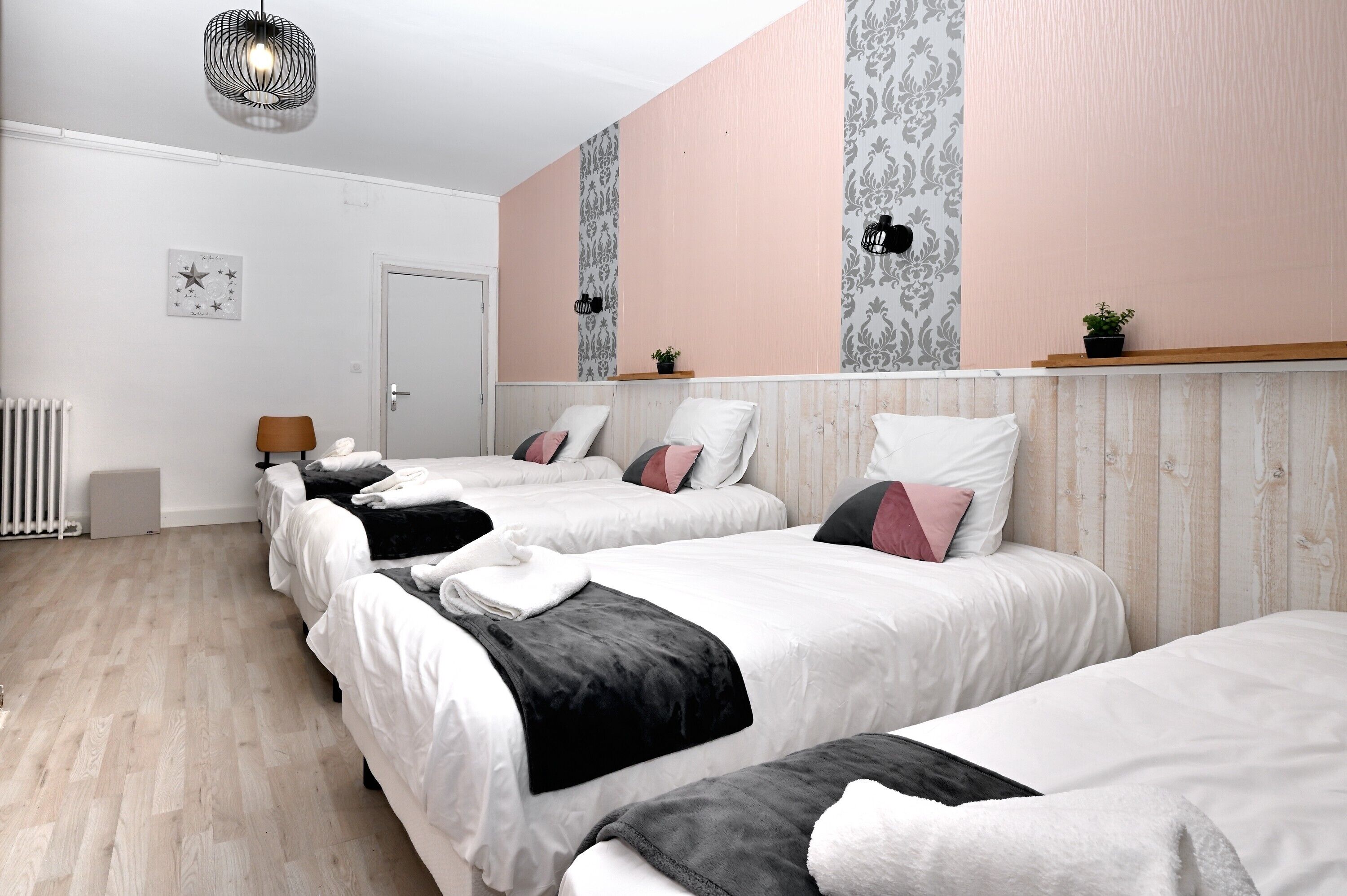 Ein Hotelzimmer mit drei Betten, einem Heizkörper, einer Tür und einer Wand mit einem strukturierten Wandpapier-Muster.