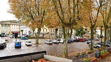 A parking lot with cars and trees, buildings in the background, and a wet ground.
