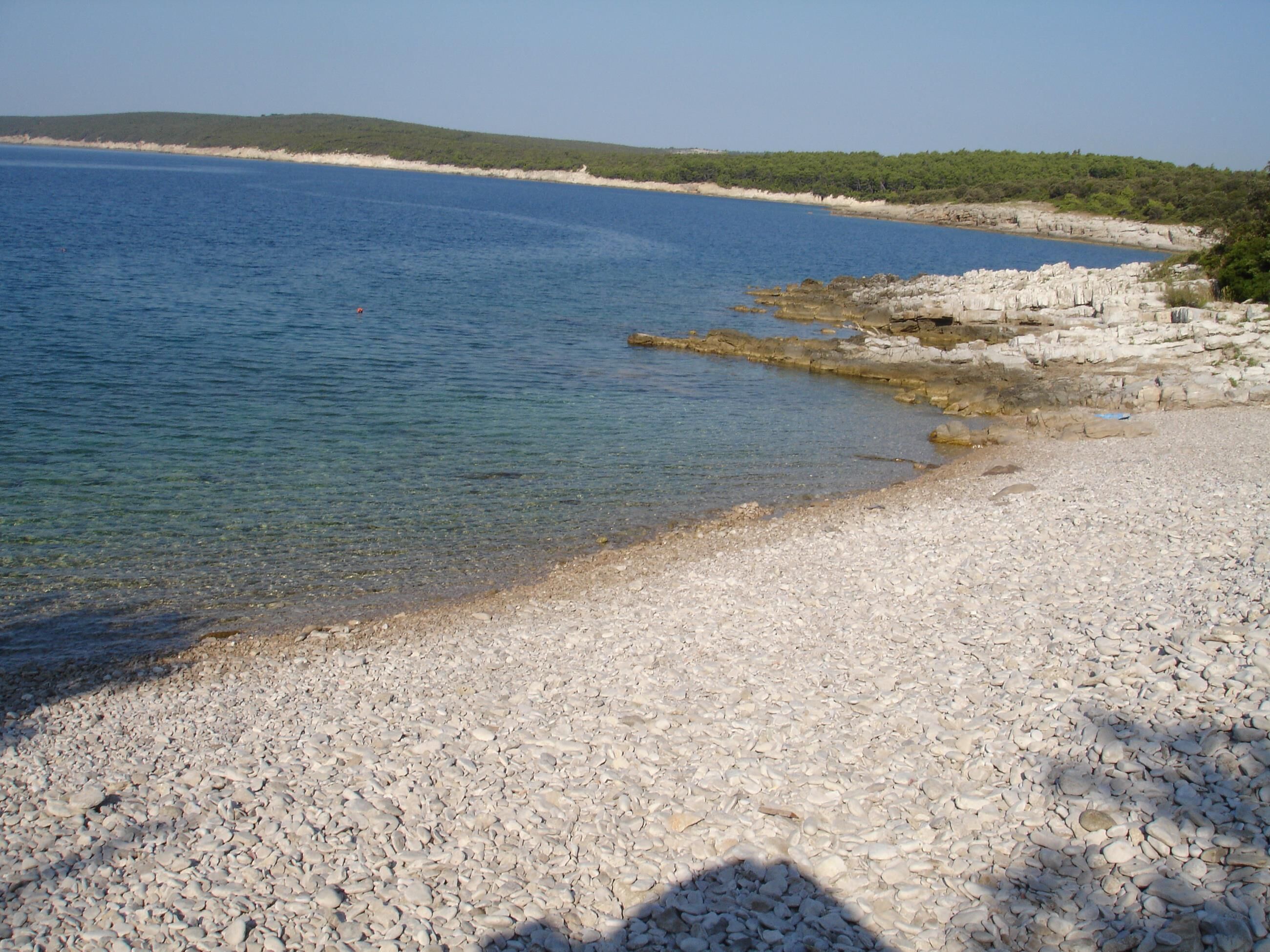 Ein Kiesstrand mit klarem Wasser und Felsformationen.