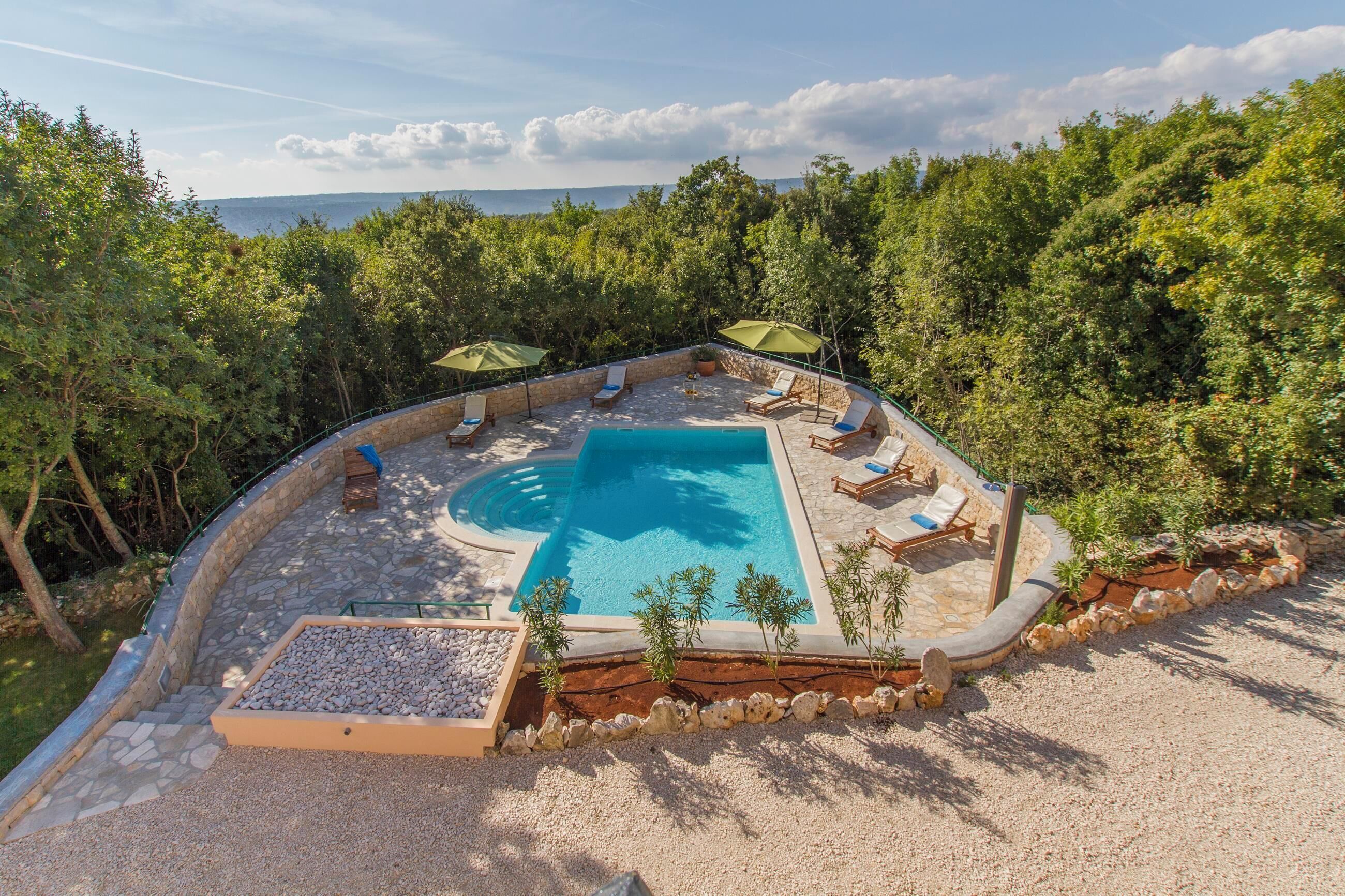 Une piscine entourée de chaises longues et de parasols, avec en arrière-plan une forêt dense et un ciel dégagé.