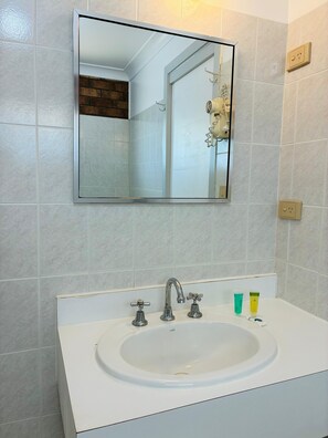 Un baño con un lavamanos blanco, un espejo y un perchero para toallas.