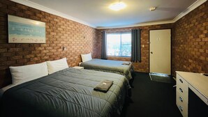 Ein Zimmer mit zwei Betten, einem Schreibtisch, einem Fenster mit Vorhängen und einer Ziegelwand.