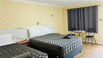 A hotel room with two beds, a small table, two chairs, a brick-patterned wall, and a curtain.