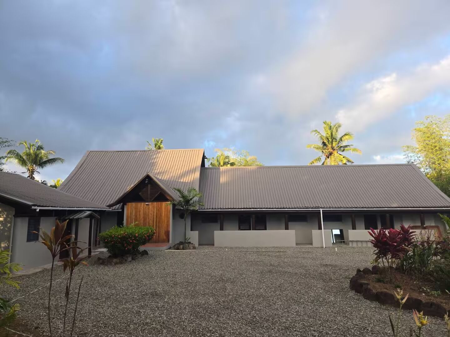 A modern two-story building with a gravel driveway and tropical landscaping.