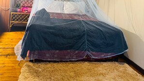 Uma cama com mosquiteiro, piso de madeira e tapete felpudo.