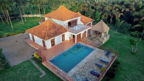 Une maison à deux étages avec une piscine, une structure à toit de chaume et un patio en pierre.