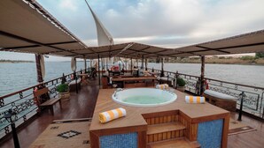 A deck with a hot tub, wooden seating, and a view of the water. - Sonesta Dahabeya Amirat I - Nile Cruise Ship - 7 nights from Luxor every Saturday  (Luxor)