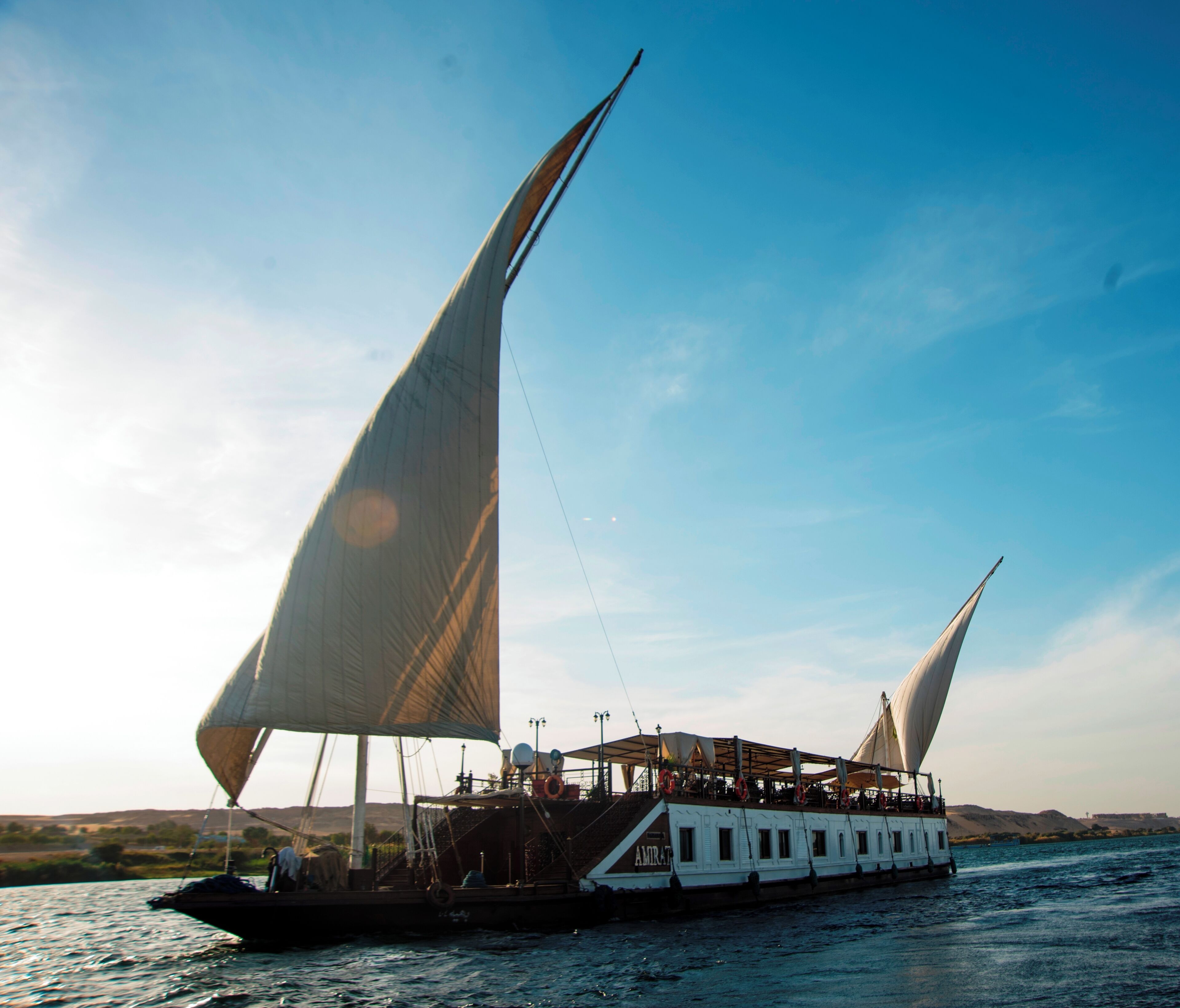 A large, white riverboat with multiple decks and a covered upper deck, sailing on a calm river.