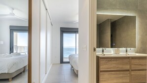 A modern hotel room with a large bed, a bathroom with a wooden vanity, and a view of the sea through a large window. - RentitSpain – Sea Views, Pool & Private Beach (Granada)