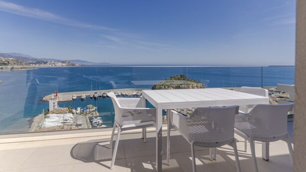 A balcony with a white table and chairs overlooking a marina and the sea. - RentitSpain – Sea Views, Pool & Private Beach (Granada)