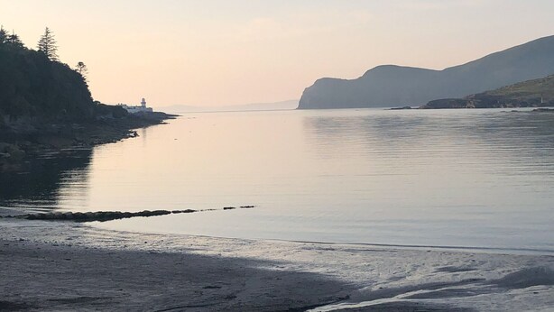 A calm river with a lighthouse on a rocky shore, surrounded by hills.
