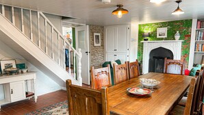 A dining area with a wooden table, chairs, a patterned rug, a staircase, and a fireplace. - Ballylusky Holiday Home (Ballydavid)