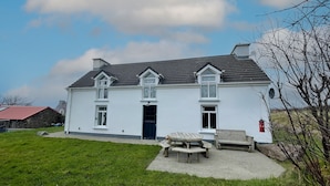 A two-story white house with a grey roof, a front door, and a small porch with a bench. - Ballylusky Holiday Home (Ballydavid)